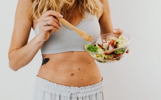 Young woman in sports attire holding a fresh salad bowl, promoting a healthy lifestyle.