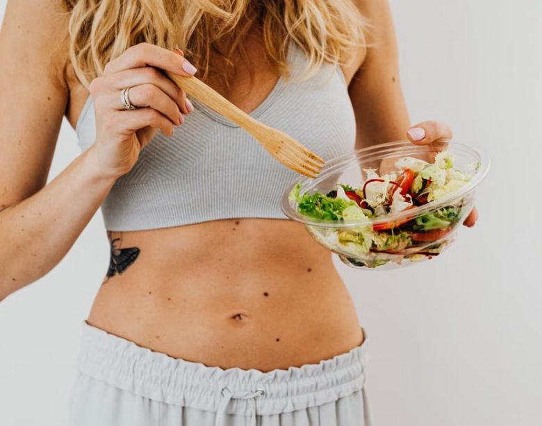 Young woman in sports attire holding a fresh salad bowl, promoting a healthy lifestyle.