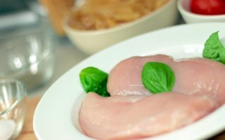 Close-up of raw chicken breasts on a plate with basil leaves, ideal for culinary themes.
