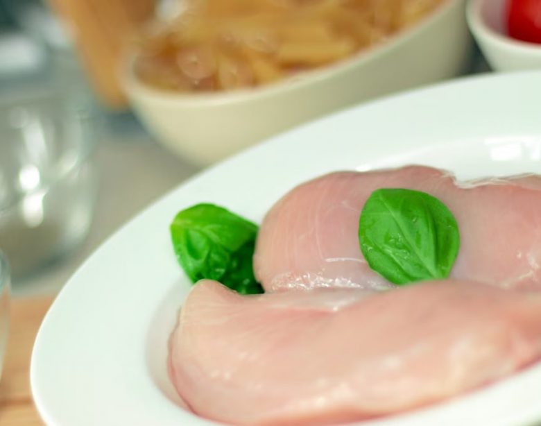 Close-up of raw chicken breasts on a plate with basil leaves, ideal for culinary themes.