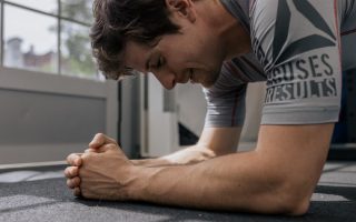 Focused man doing a plank exercise inside a gym for a core workout.