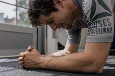 Focused man doing a plank exercise inside a gym for a core workout.