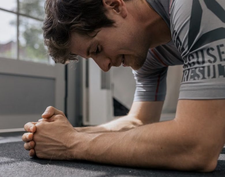 Focused man doing a plank exercise inside a gym for a core workout.